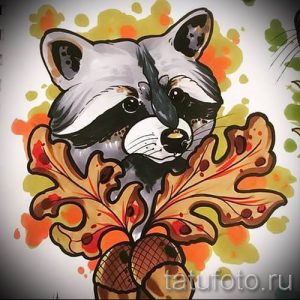 Фото тату енота, держащего желуди, выполненное в акварельном стиле с использованием теплых осенних оттенков. Нежный и оригинальный эскиз татуировки.