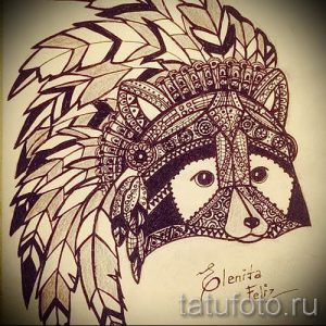Фото эскиза татуировки енота в индейском стиле, украшенного перьями и геометрическими узорами. Черно-белый рисунок.