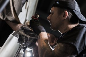 Фотография процесса нанесения татуировки: мастер тату сосредоточенно работает над рисунком на руке клиента, используя тату-машинку.