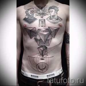 Большая татуировка на груди с изображением нескольких пирамид, портретов и геометрических фигур. Рисунок татуировки выполнен в черно-белых тонах с использованием различных техник штриховки.