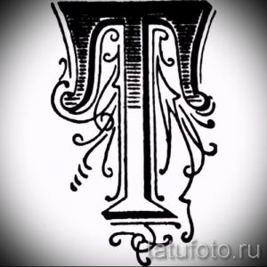 Фото тату: стилизованная буква 'T' с изящными завитушками и узорами, выполненная в черном цвете. Подходит для инициалов и монограмм.