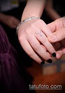 Фото тату: миниатюрный крест, выполненный тонкими линиями, на пальце руки. Деликатный и изящный рисунок татуировки.