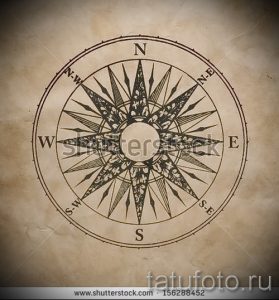 Фото татуировки с изображением старинного компаса на фоне пергамента. Рисунок выполнен в коричневых тонах и имеет эффект состаренности.