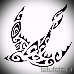 Фото татуировки ласточки, выполненной в стиле трайбл. Эскиз состоит из черных узоров и спиралей, создающих динамичный и мощный образ.