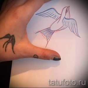 Фото миниатюрной татуировки ласточки на запястье. Рисунок выполнен в черно-серых тонах, с детальной проработкой крыльев и тела птицы.