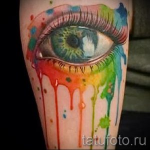 Фото тату: реалистичный глаз, из которого стекают разноцветные краски, образуя радугу. Выполнено в технике акварели с яркими, насыщенными цветами.