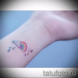 Небольшая цветная татуировка на запястье с изображением облака, радуги и капель дождя. Милый и нежный рисунок татуировки.