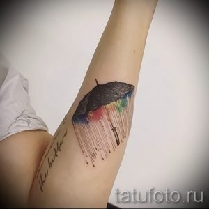 Фото акварельной татуировки на руке с изображением черного зонта, из которого льется радуга. Нежный и романтичный дизайн.