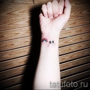 Фото минималистичной татуировки на запястье с изображением радуги и двух силуэтов людей. Простой дизайн и символическое значение.