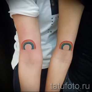Фото парных татуировок с изображением полукругов радуги на предплечьях двух людей. Яркие цвета и минималистичный дизайн.