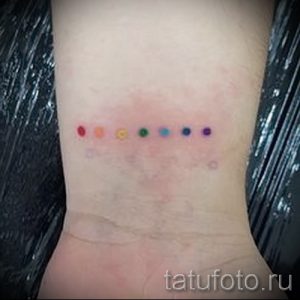 Фото тату маленькой радуги из точек на запястье. Минималистичный дизайн, яркие цвета, нежный и стильный аксессуар.