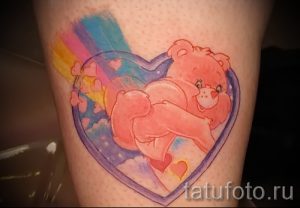 Фото тату с розовым медвежонком Care Bear, окруженным радугой и сердечками на ноге.