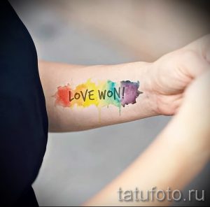 Фото акварельной тату на предплечье с надписью 'LOVE WON!' и разноцветными брызгами.