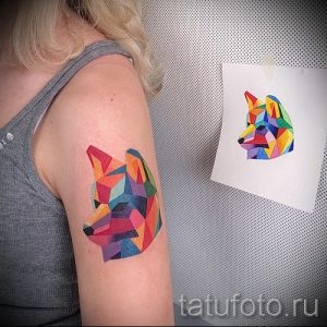 Татуировка на плече с изображением лисы, выполненной в геометрическом стиле и ярких цветах. Оригинальный рисунок татуировки.