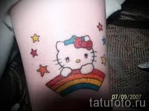 Небольшое тату Hello Kitty, сидящей на радуге, украшенное звездочками. Яркий и милый рисунок татуировки для девочек.