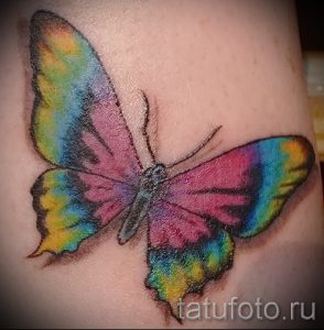 Фото тату бабочки с радужными крыльями на руке. Рисунок татуировки выполнен в ярких, насыщенных цветах, создавая эффектный и привлекательный образ.