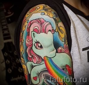 Фото тату: изображение мультяшной лошадки My Little Pony с радугой на плече. Яркий и красочный рисунок татуировки, выполненный в мультяшном стиле.