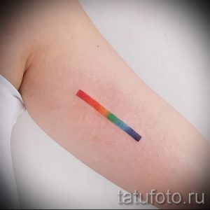 Фото тату минималистичной радуги на руке. Тонкая линия, состоящая из семи цветов, современный и стильный дизайн.
