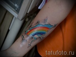 Фото тату радуги, прорывающейся сквозь потрескавшуюся кожу на руке. Яркие цвета радуги контрастируют с серыми трещинами, создавая эффект объема.