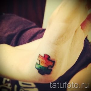 Фото тату: яркий кусочек пазла с градиентом от красного к зеленому на женском запястье. Небольшой рисунок татуировки.