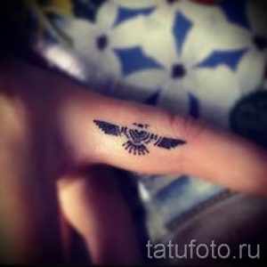 Фотография небольшой татуировки в виде крыльев, расположенной на пальце руки. Изящный рисунок, выполненный в черном цвете.