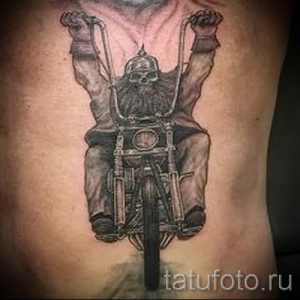 Фото тату: детализированная татуировка на боку с изображением мотоциклиста в шлеме-черепе, едущего на мотоцикле.