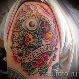 Фото тату: красочная татуировка на плече с изображением мотоциклетного двигателя, украшенного крыльями и розами, и надписью 'Freedom'.