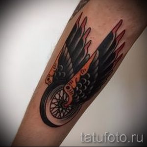 Фото тату на руке в стиле олдскул с изображением крыла и мотоциклетного колеса. Яркие цвета и четкие контуры.