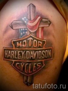 Фото тату на плече с изображением логотипа Harley-Davidson, стилизованного под американский флаг и крест.