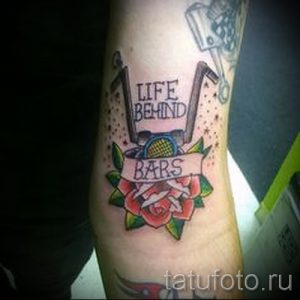Фото тату на предплечье с изображением розы, решеток и надписи 'Life Behind Bars'. Яркий и традиционный рисунок.