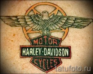 Фото тату логотипа Harley-Davidson на плече. Изображение включает в себя крылатого орла и надпись 'MOTOR HARLEY-DAVIDSON CYCLES'.