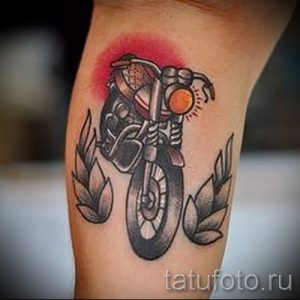 Фото тату: классический мотоцикл с красным фоном на руке. Использованы цвета: черный, серый и красный. Детализированный рисунок татуировки.