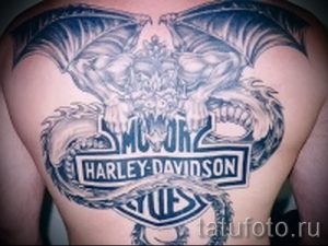 Фото тату: огромный дракон с распахнутыми крыльями и логотипом Harley-Davidson на спине. Использованы только черные тона. Детализированный рисунок татуировки.