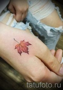 Фото тату маленького кленового листа на руке. Красные и коричневые оттенки, реалистичный рисунок татуировки.