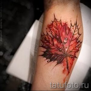 Фото тату кленового листа с каплями росы на руке. Красные и коричневые оттенки, реалистичный рисунок татуировки, выполненный в технике акварели.