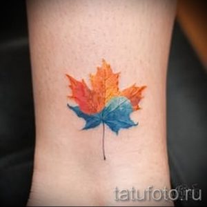 Фото тату акварельного кленового листа на запястье. Рисунок выполнен в ярких, размытых цветах, имитирующих технику акварельной живописи.