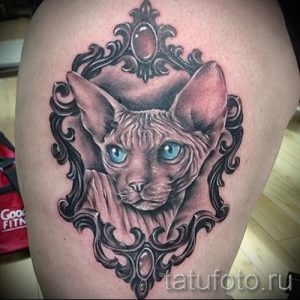 Фото тату сфинкса кошки в декоративной рамке, выполненное в реалистичном стиле с использованием оттенков серого и голубых глаз.