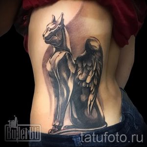 Фото тату крылатой кошки Бастет на боку, выполненное в реалистичном стиле с использованием черных и серых оттенков.