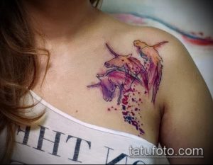 Фото тату: акварельные единороги на плече девушки. Нежные розовые и фиолетовые оттенки, брызги краски, легкий и воздушный рисунок.