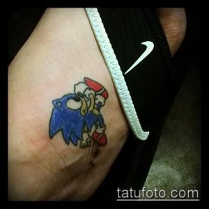Фото тату Sonic the Hedgehog в смешной позе, как будто он споткнулся. Яркие цвета и мультяшный стиль.