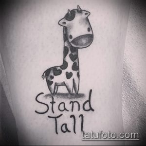 Фотография милой татуировки жирафа в мультяшном стиле с надписью "Stand Tall". Рисунок татуировки выполнен в черно-белых тонах.