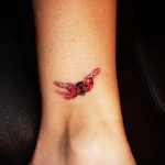 Фото миниатюрной татуировки божьей коровки на лодыжке. Нежный рисунок татуировки с реалистичными деталями и яркими цветами.