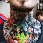 Фото тату на шее: реалистичный череп, окруженный яркими цветами и жуком, выполненный в яркой цветовой гамме.