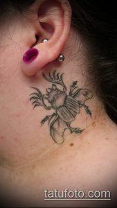 Фото небольшой татуировки жука-носорога на шее. Черно-серый рисунок с детальной проработкой рогов и крыльев.