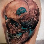 Фото тату черепа с жуком на предплечье. Реалистичный рисунок с детальной проработкой и использованием красных акцентов.