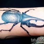 Фото татуировки синего жука на руке. Детализированный рисунок с использованием ярких синих и черных оттенков.