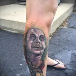 Фото татуировки с изображением персонажа Бетельгейза из фильма. Детализированный портрет на ноге, выполненный в мрачных тонах.