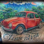 Фото тату: красный Volkswagen Beetle на фоне пейзажа, выполненный в ярких цветах. Детализированный рисунок на спине.
