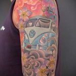 Фото яркой татуировки Volkswagen Bus, окруженного цветами сакуры на плече. Использованы пастельные тона и детализированная прорисовка.