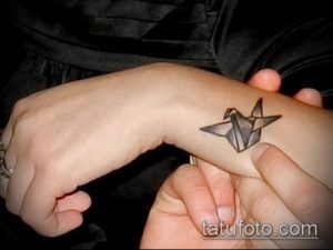 Фотография небольшой татуировки на запястье с изображением бумажного журавлика, выполненного в черно-серых тонах в стиле оригами.